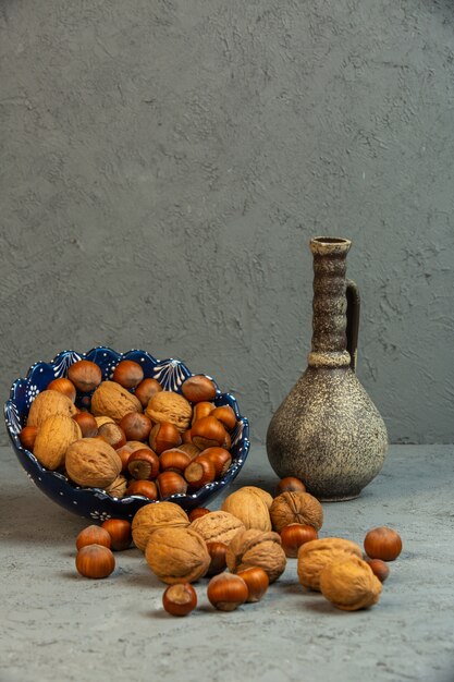 Vista frontal de nueces con avellanas en cáscara esparcidas de un jarrón con una jarra