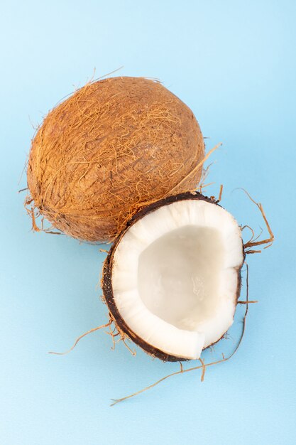 Una vista frontal de nueces de coco en rodajas y todo dulce lechoso fresco aislado en el azul helado