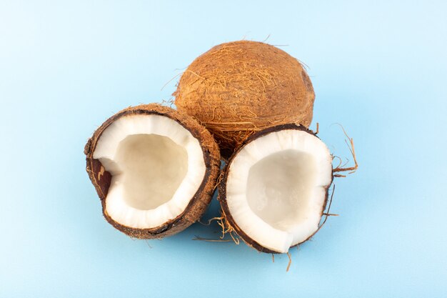 Una vista frontal de nueces de coco en rodajas y todo lechoso dulce fresco aislado en el fondo azul helado tuerca de frutas exóticas tropicales