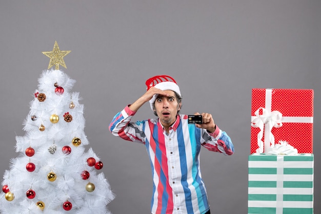 Vista frontal observando al hombre poniendo la mano en la frente de pie cerca del árbol de Navidad blanco