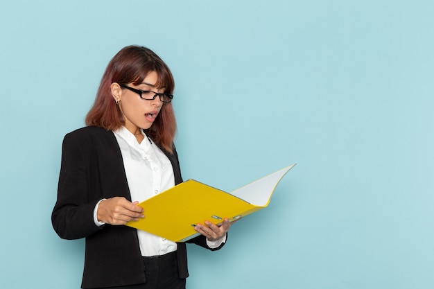 Vista frontal oficinista femenina leyendo documento amarillo sobre la superficie azul