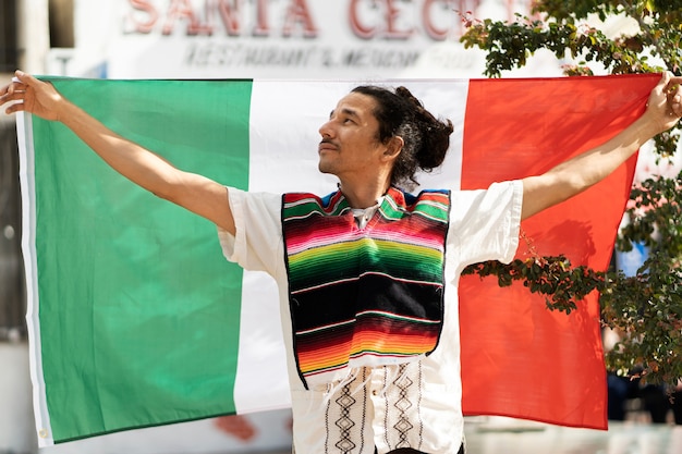Vista frontal orgulloso joven sosteniendo la bandera mexicana