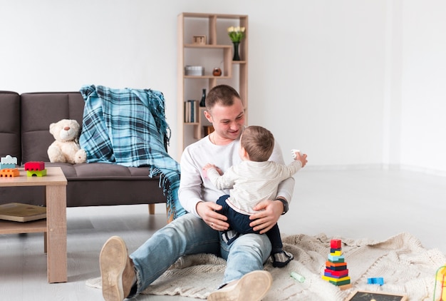 Vista frontal del padre con bebé y juguetes en casa