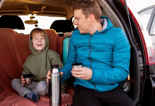 Vista frontal de padre e hijo en el coche bebiendo té durante un viaje por carretera