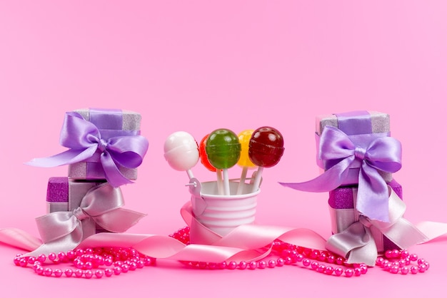 Una vista frontal de paletas y cajas de regalo púrpura cajas aisladas en rosa, fiesta de celebración de cumpleaños