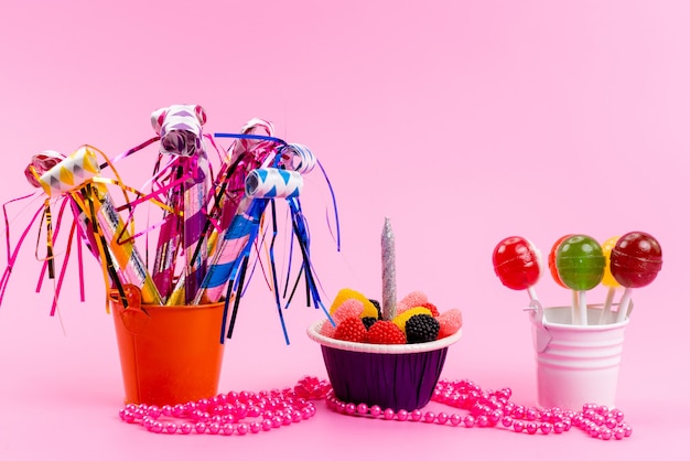 Una vista frontal de paletas y mermeladas dentro de pequeños baldes junto con silbidos de cumpleaños en rosa, dulce azúcar de caramelo