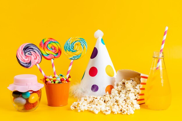 Una vista frontal de palomitas de maíz y dulces con gorra de cumpleaños cóctel frío amarillo sobre amarillo