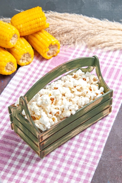 Vista frontal de palomitas de maíz frescas dentro de una caja de madera en el piso oscuro, palomitas de maíz de snack