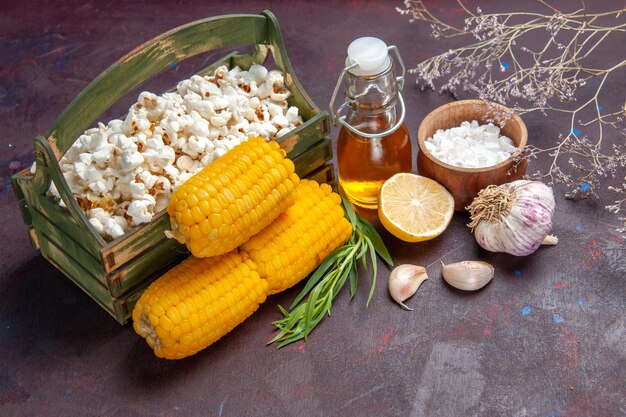 Vista frontal de palomitas de maíz frescas con granos amarillos en palomitas de maíz de aceite de película de snack de maíz de superficie oscura