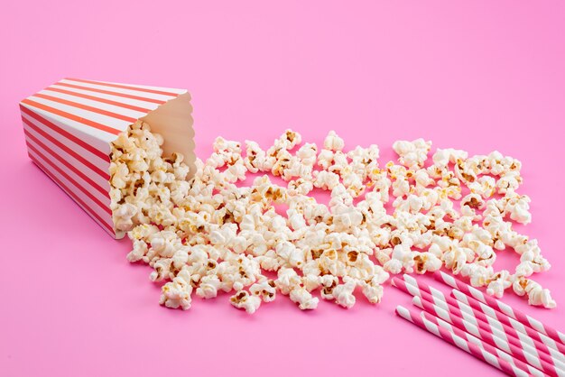 Una vista frontal de palomitas de maíz frescas saladas esparcidas sobre rosa, semilla de maíz de snack de película