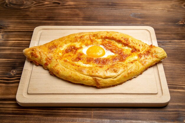 Vista frontal de pan horneado con huevo cocido en la superficie de madera bollo de pan comida huevo masa para el desayuno