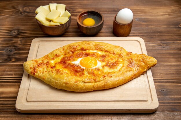 Vista frontal de pan recién horneado con huevo cocido en un escritorio de madera marrón, masa de pan, pan, desayuno, huevo, comida