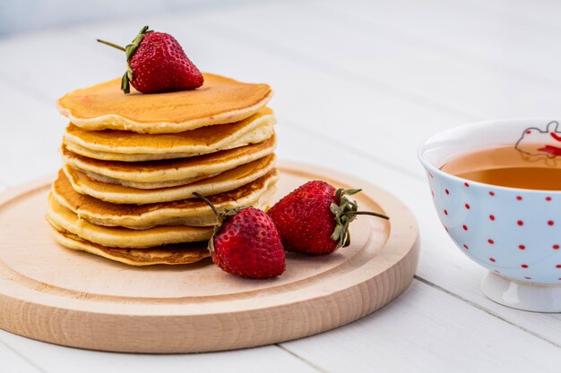 Vista frontal de panqueques con fresas en una bandeja con una taza de té