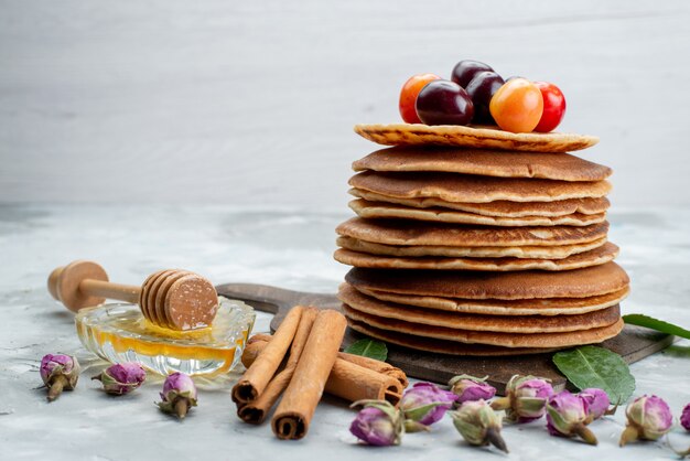 Una vista frontal de panqueques redondos horneados y deliciosos con cerezas y canela en la mesa de luz pastel de frutas