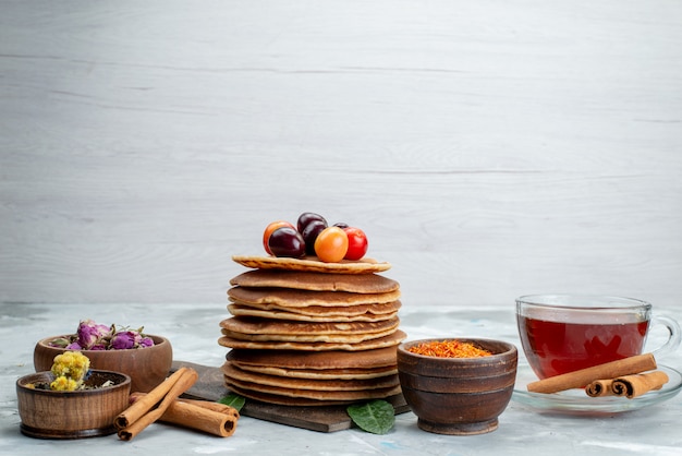 Una vista frontal panqueques redondos horneados y deliciosos con cerezas, canela y té en la mesa de luz pastel de frutas