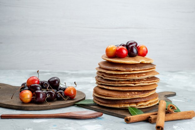 Una vista frontal panqueques redondos horneados y deliciosos con cerezas en la mesa de luz pastel postre de frutas