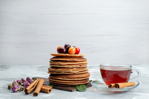 Una vista frontal panqueques redondos horneados y deliciosos con té de cerezas en la mesa de luz pastel de frutas