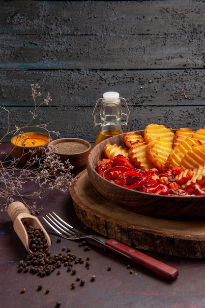 Vista frontal de papas al horno con verduras cocidas y condimentos en un espacio oscuro