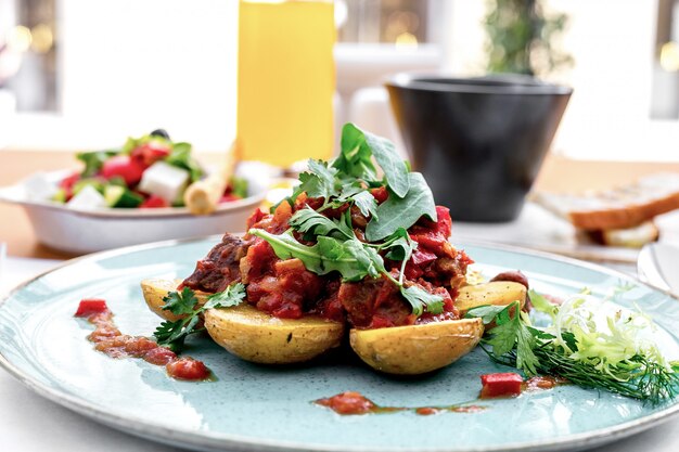 Vista frontal de papas con carne en salsa de tomate con rúcula y ensalada griega sobre la mesa