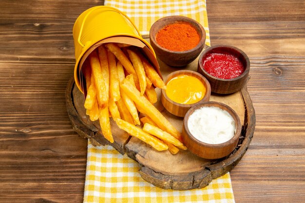 Vista frontal de papas fritas con condimentos en el escritorio de madera, almuerzo, merienda, merienda