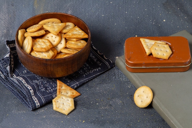 Vista frontal de papas fritas y galletas dentro de la placa marrón en la superficie gris