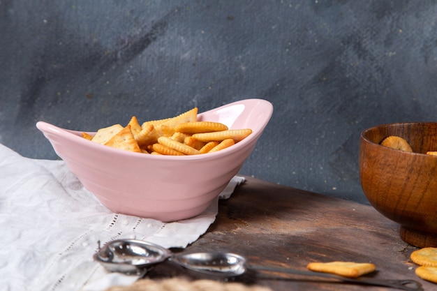 Vista frontal de papas fritas y galletas dentro de la placa rosa en la superficie gris