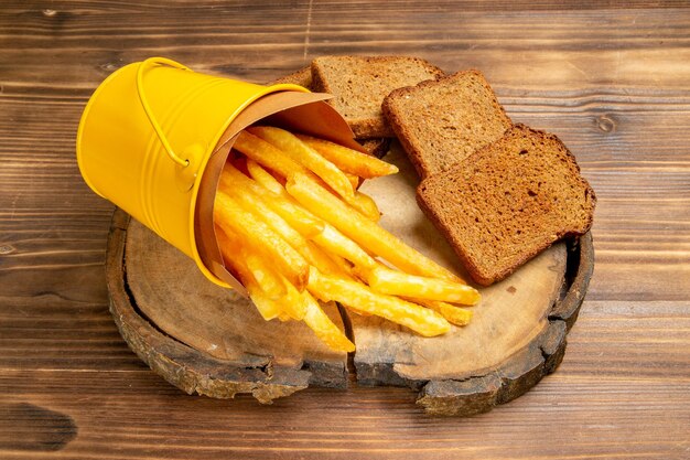 Vista frontal de las papas fritas con hogazas de pan oscuro en el escritorio marrón pan de comida rápida de papa