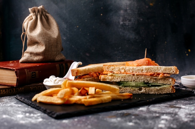 Vista frontal papas fritas junto con sándwiches en el escritorio negro y superficie gris