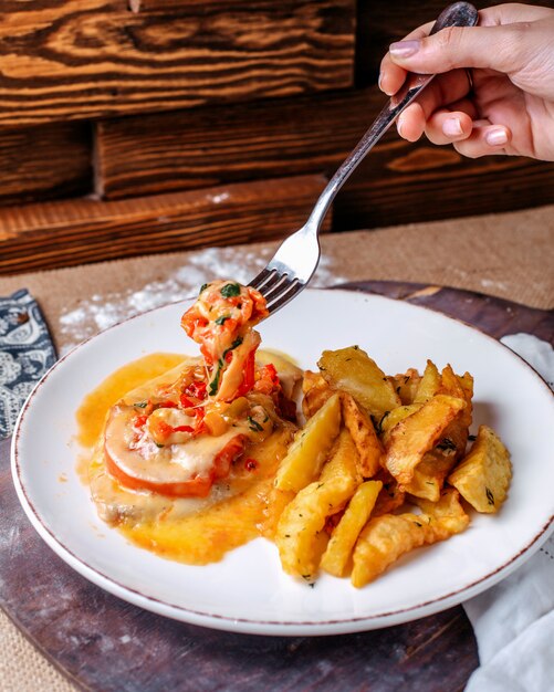 Vista frontal papas fritas junto con verduras dentro de un plato blanco en el piso marrón