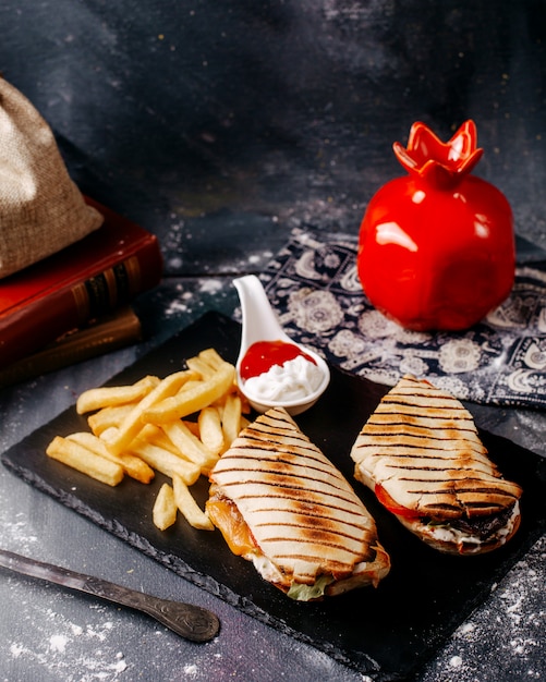 Vista frontal papas fritas con rodajas de sándwich dentro de la placa negra en el escritorio gris