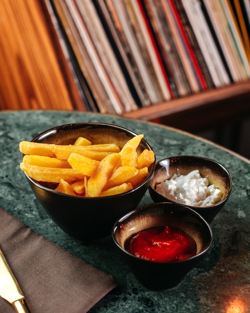 Una vista frontal papas fritas sabroso junto con salsa de tomate y mayonesa en el escritorio verde