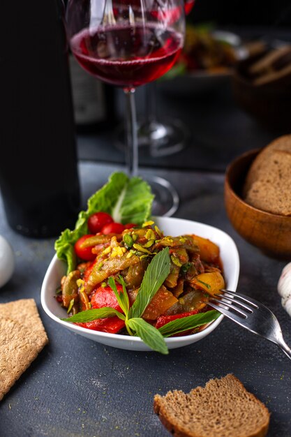 Una vista frontal papas trituradas junto con verduras en rodajas hojas verdes dentro del plato blanco junto con patatas fritas vino tinto en el escritorio gris vitaminas vegetales