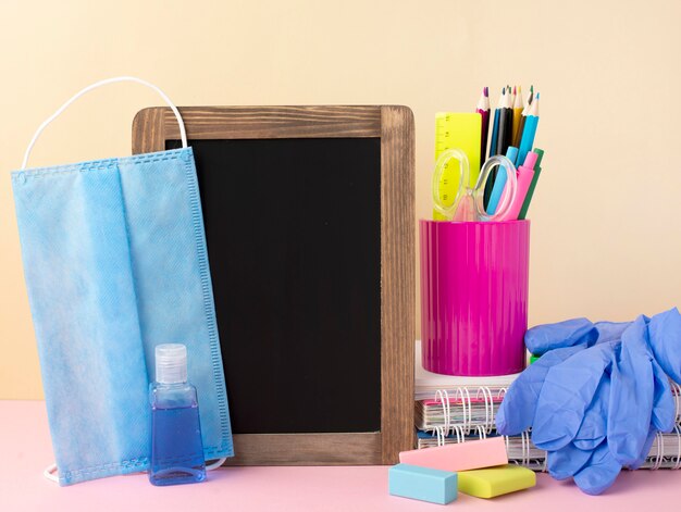 Vista frontal de papelería de regreso a la escuela con máscara médica y pizarra