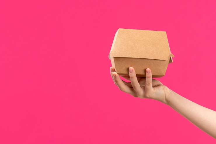 Foto gratuito una vista frontal del paquete mano que sostiene el paquete marrón mano femenina color de fondo rosado comer alimentos