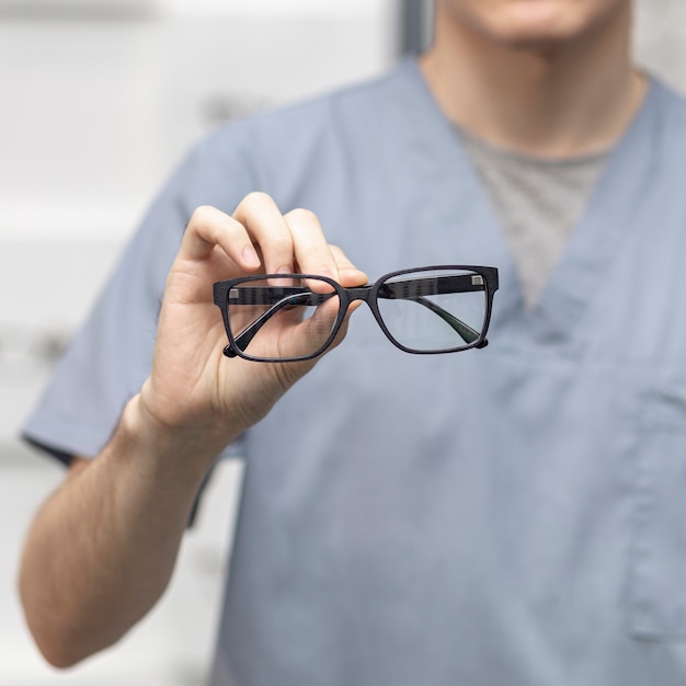 Vista frontal de un par de gafas sostenidas por un hombre desenfocado