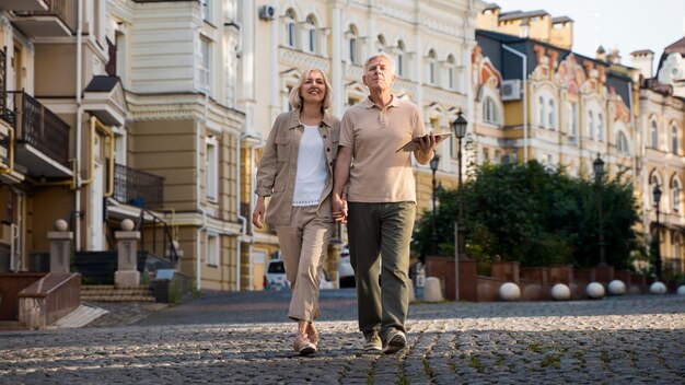 Vista frontal de la pareja de ancianos a dar un paseo por la ciudad con tableta