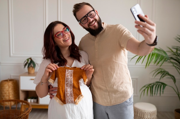 Foto gratuita vista frontal pareja anunciando embarazo con teléfono inteligente