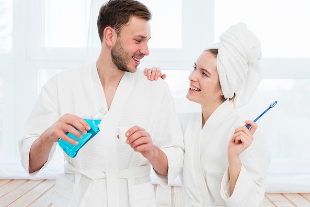 Vista frontal de la pareja en batas de baño con enjuague bucal y cepillo de dientes