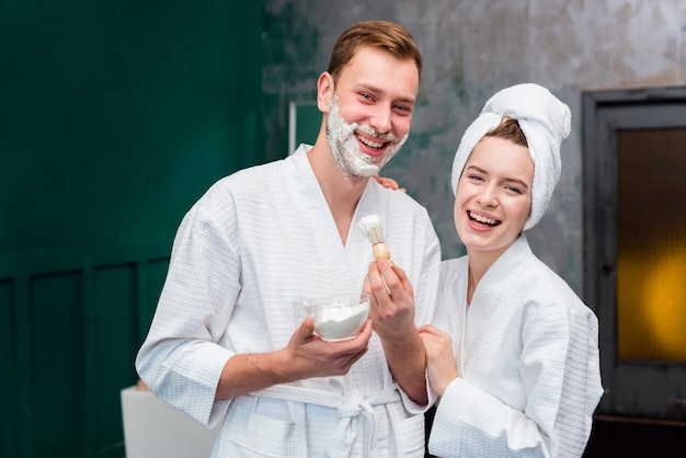 Vista frontal de la pareja en batas de baño con espuma de afeitar