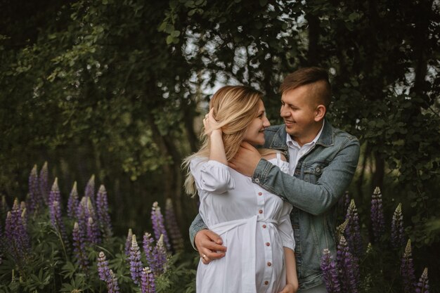 Vista frontal de la pareja feliz con una sonrisa sincera en el parque verde con lupino violeta, esperando bebé