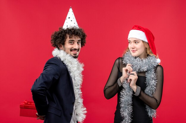 Vista frontal pareja joven celebración de año nuevo presente en la pared roja emociones aman la navidad