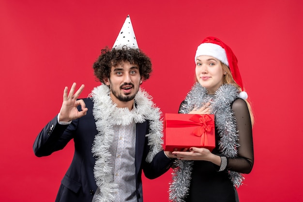 Vista frontal pareja joven con presente celebrando en la pared roja fiesta amor de navidad