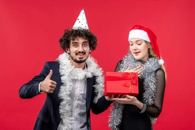 Vista frontal pareja joven con presente celebrando en la pared roja fiesta amor de navidad