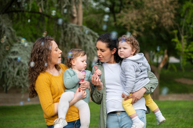 Vista frontal de la pareja lgbt al aire libre con niños y pompas de jabón