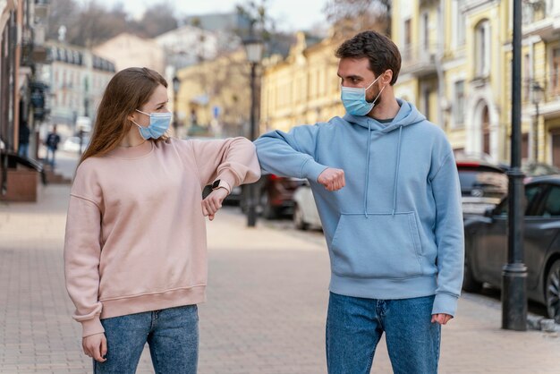 Vista frontal de la pareja con máscara médica utilizando el saludo del codo