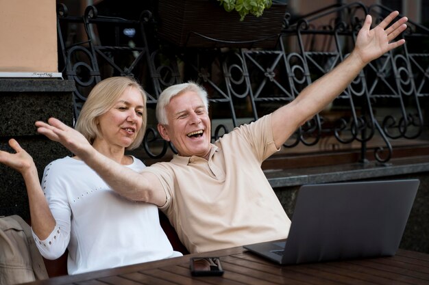 Vista frontal de la pareja mayor que tiene una videollamada en la computadora portátil mientras está al aire libre