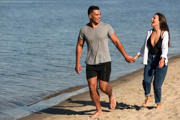 Vista frontal de la pareja romántica tomados de la mano mientras da un paseo por la playa