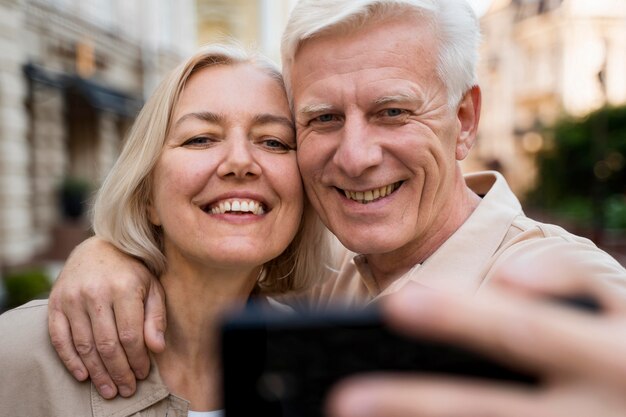 Vista frontal de la pareja senior sonriente tomando un selfie mientras está en la ciudad