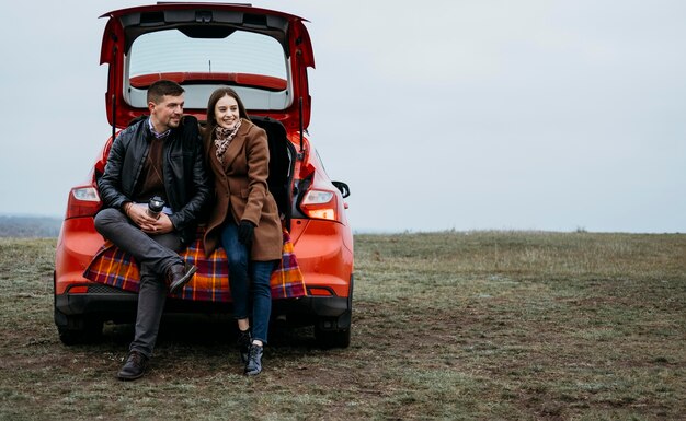 Vista frontal de la pareja sentada en el maletero del coche con espacio de copia