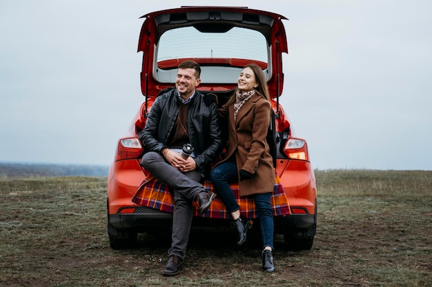 Vista frontal de la pareja sentada en el maletero del coche